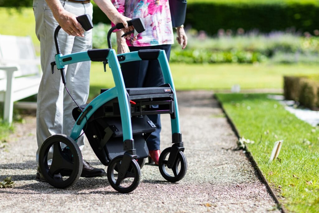 Senior adults walking with a rollator along a park path on a sunny day.